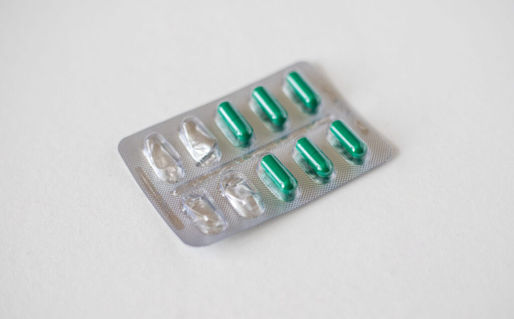 Semi-empty metal blister pack with green capsules isolated on white background. Metal blister for capsules